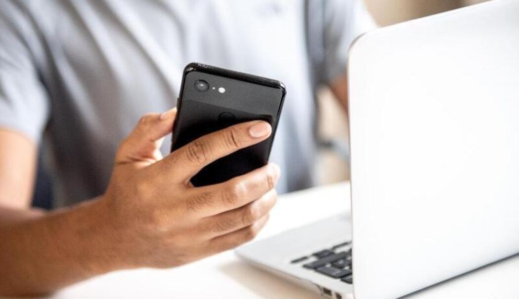 Mann mit Handy in der Hand vor einem Laptop