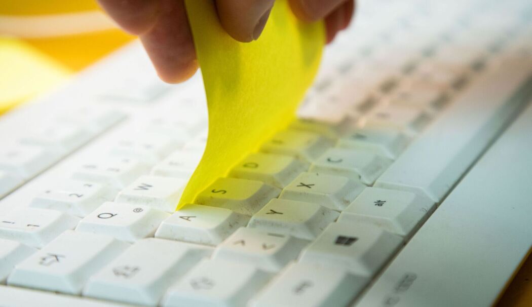 Klebezettel wird zwischen die Tastenreihen einer Tastatur gezogen