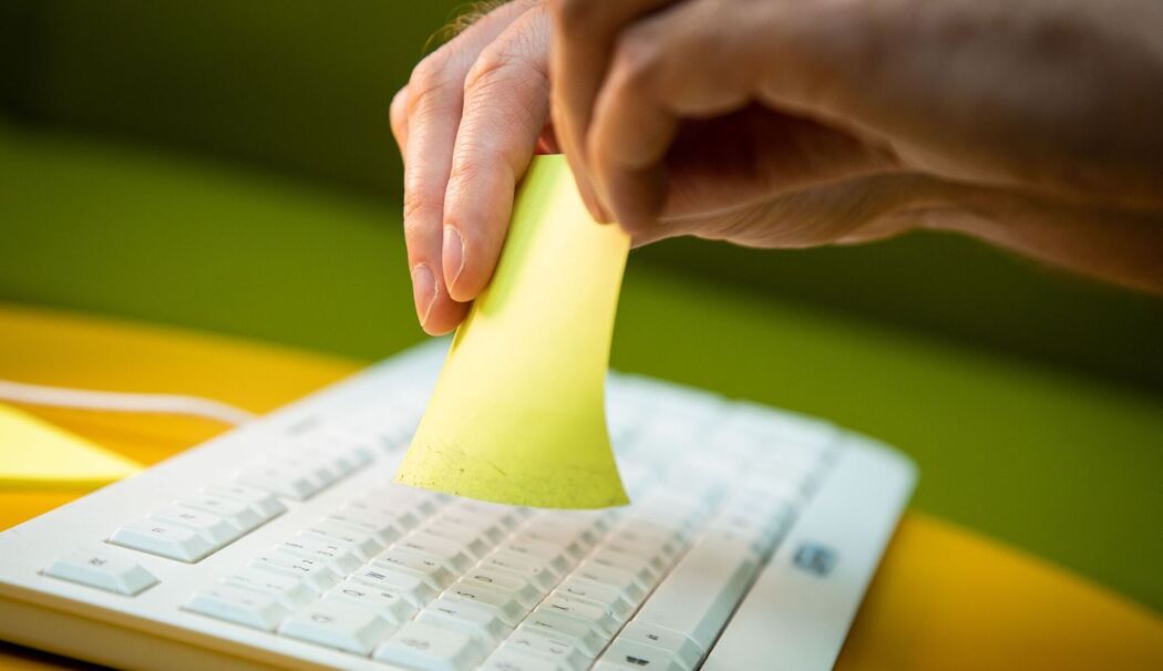Mann nutzt zum Reinigen der Tastatur einen Klebezettel