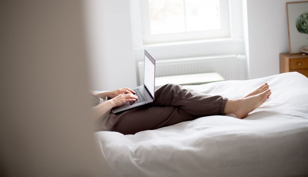 Eine Frau sitzt mit Laptop auf einem Bett