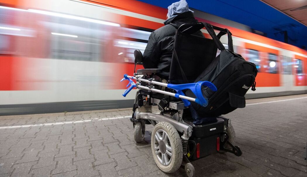 Mann im Rollstuhl steht am Bahnhof an einem Gleis