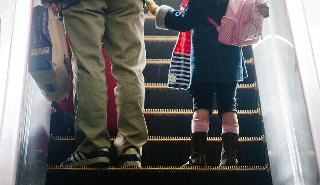 Mädchen steht neben ihrem Vater auf einer Rolltreppe