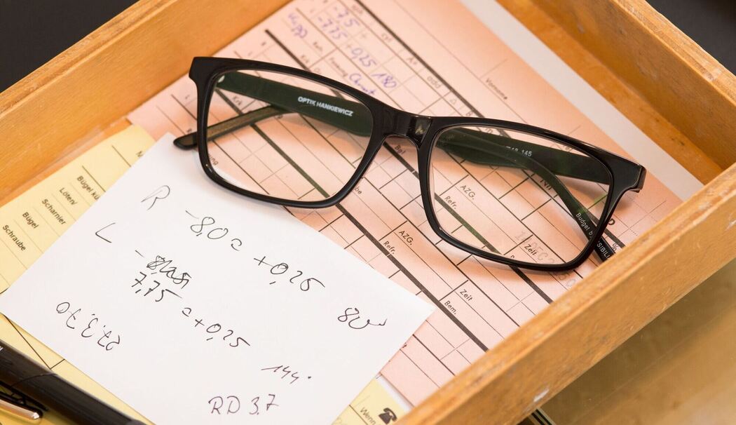 Zettel mit den Messwerten der Sehstärke liegt neben einer Brille