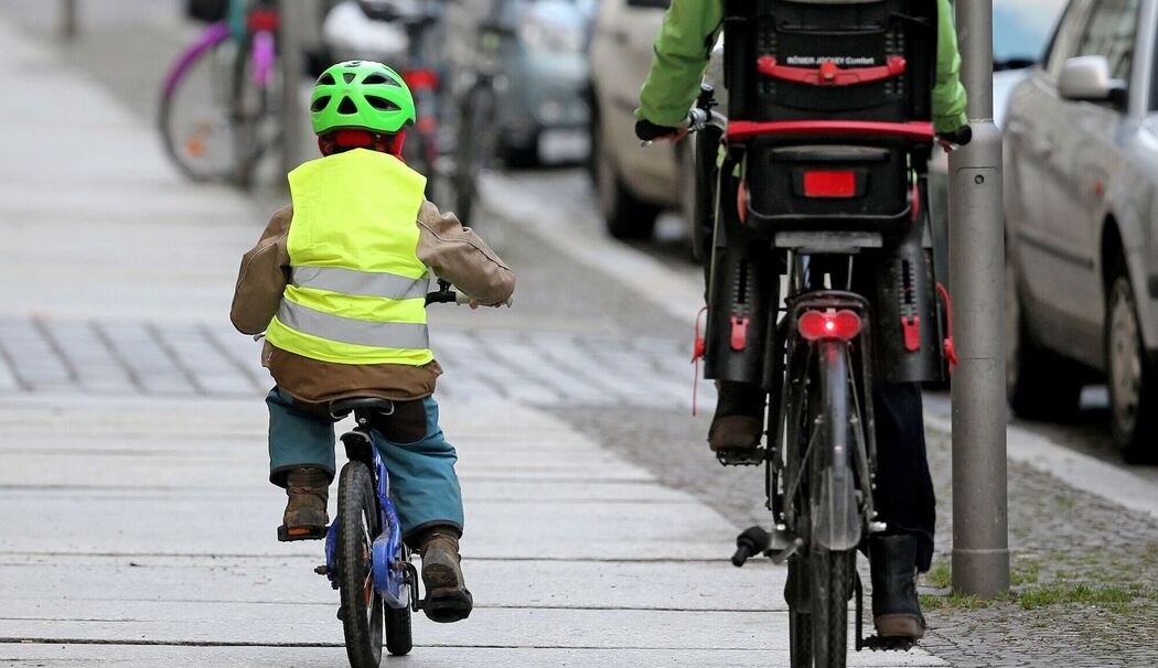 Ein Kind fährt mit dem Rad auf dem Fußweg neben einem Elterteil