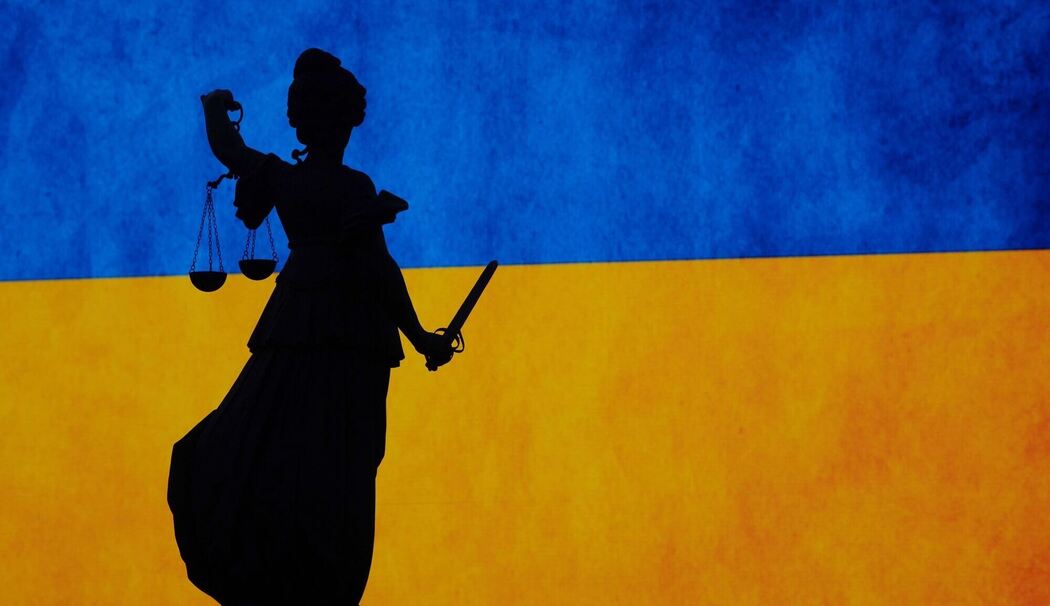 Eine Justitia-Figur vor der ukrainischen Flagge
