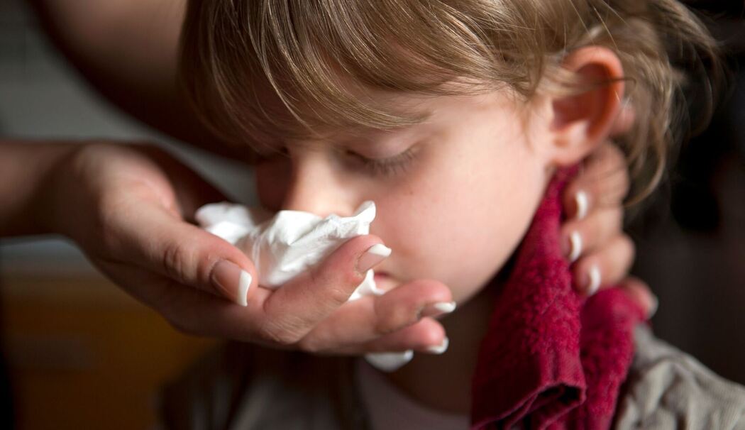 Ein Kind mit Nasenbluten hat Handtuch im Nacken