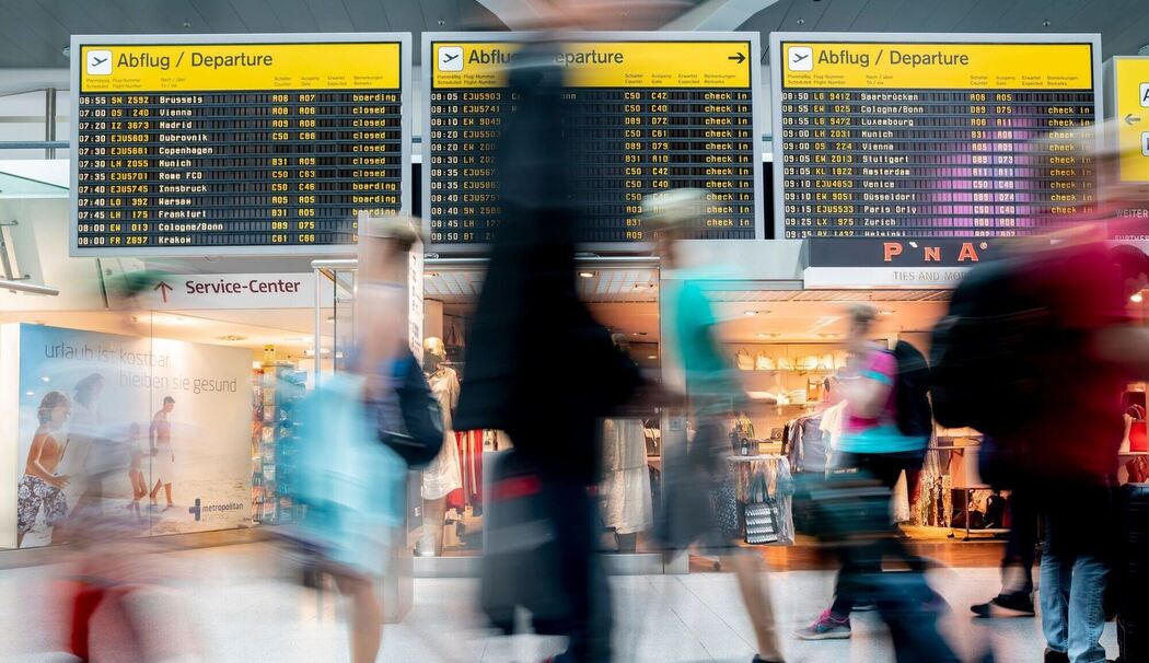 Passagiere laufen am Flughafen vor der Anzeigetafel