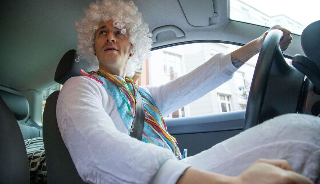 Mit einem Kostüm bekleideter Mann sitzt in einem Auto