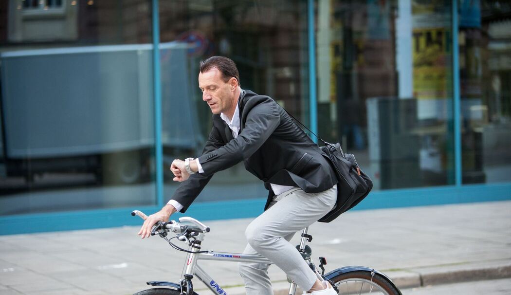 Mann fährt mit Fahrrad durch Stadt und guckt auf Uhr
