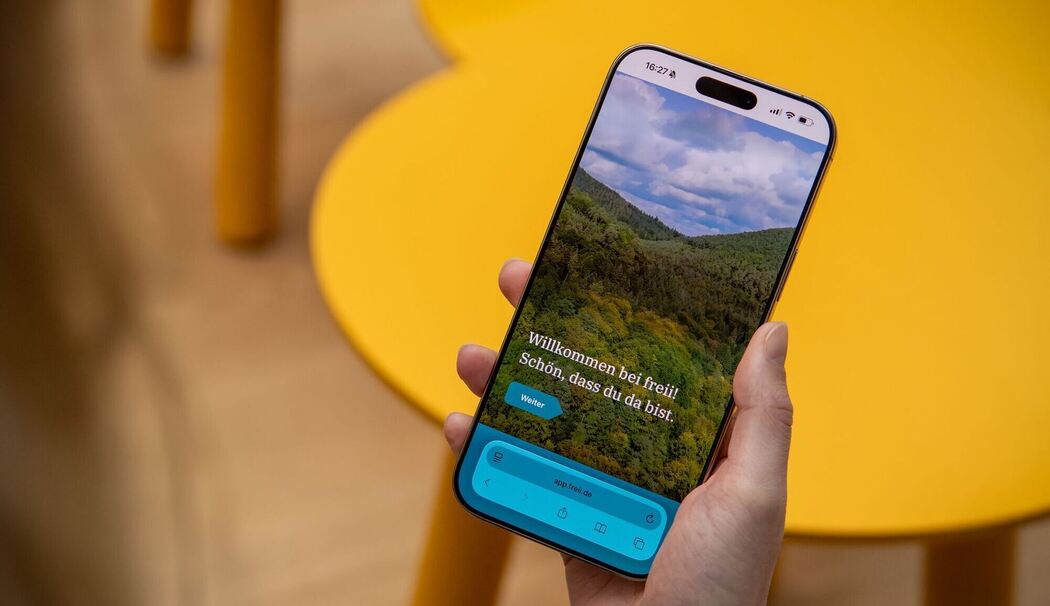 Eine Frau haelt ein Handy mit der Web-App «freii» in der Hand