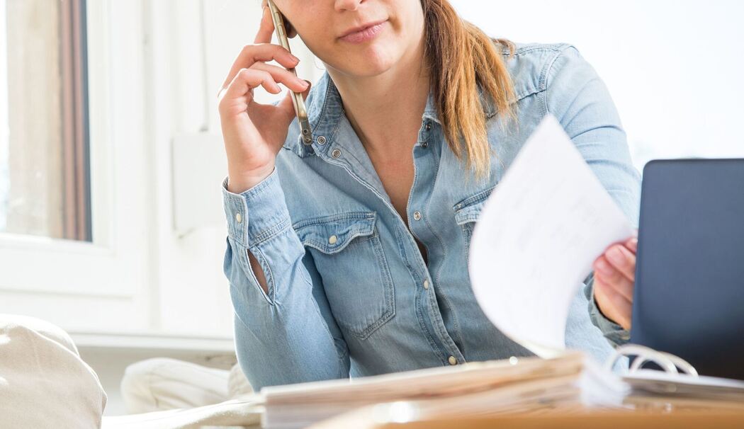 Eine Frau telefoniert und liest Unterlagen durch