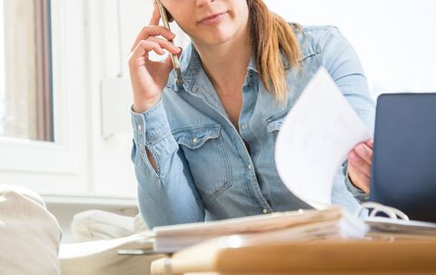 Eine Frau telefoniert und liest Unterlagen durch