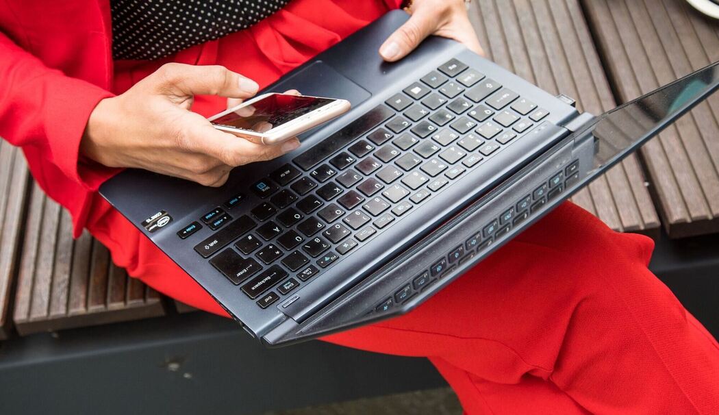Eine Frau sitzt mit Smartphone und Laptop auf einer Bank