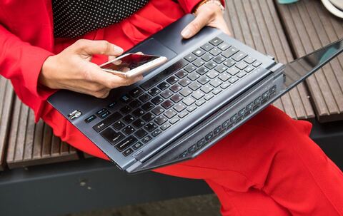 Eine Frau sitzt mit Smartphone und Laptop auf einer Bank
