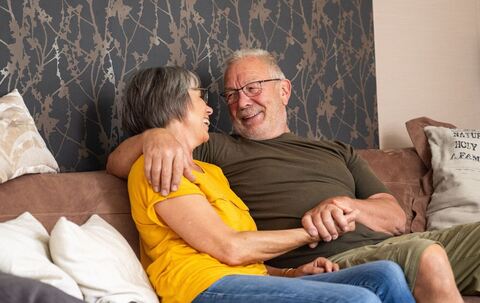 Älteres Paar sitzt lächelnd auf einer Couch