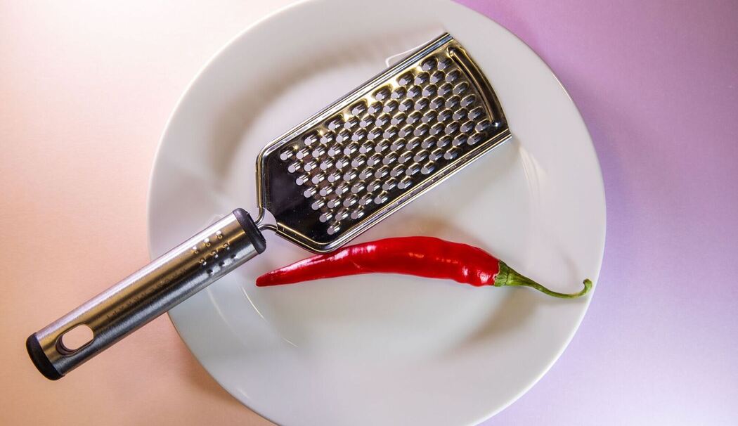 Chilischote liegt neben einer Küchenreibe