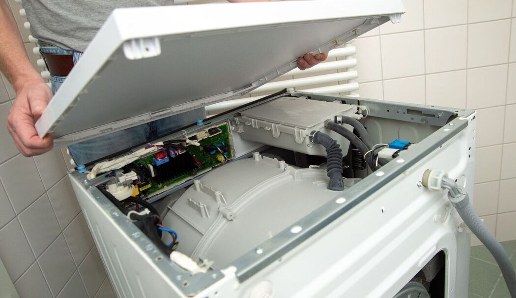 Ein Mann öffnet eine defekte Waschmaschine Ein Mann öffnet eine defekte Waschmaschine