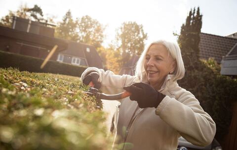 Eine ältere Dame schneidet eine Hecke