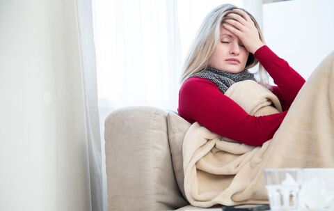 Eine Frau sitzt krank auf einem Sofa 