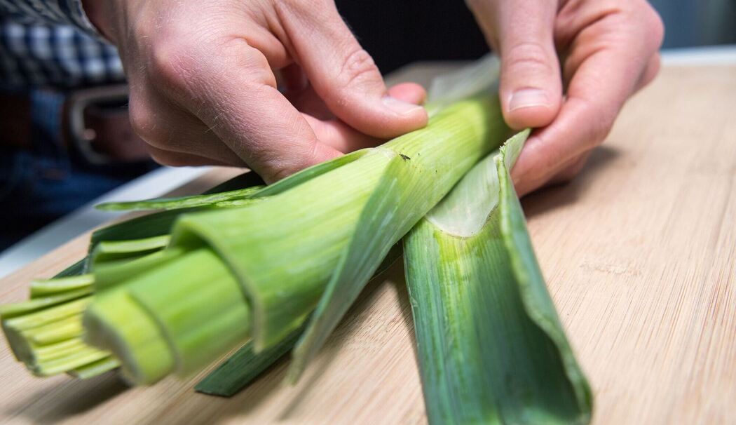 Mann entfernt die äußeren Blätter einer Lauchstange Mann entfernt die äußeren Blätter einer Lauchstange