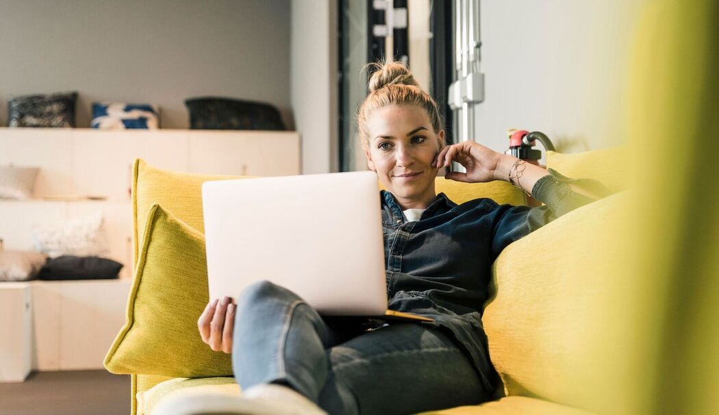 Frau sitzt mit Laptop auf einer Couch