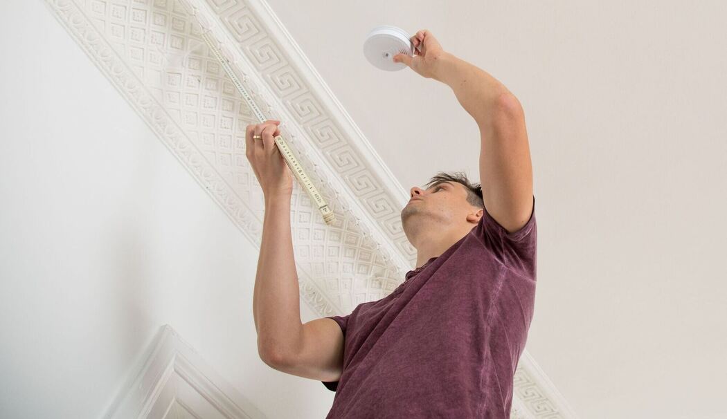 Ein Mann bringt einen Feuermelder an