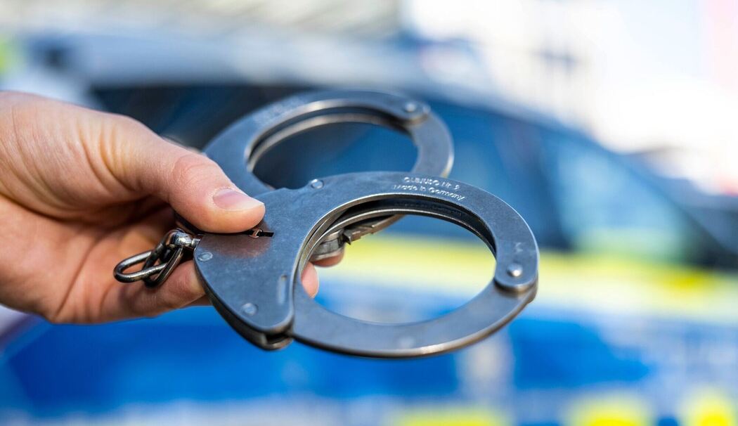 Handschellen vor Polizeiwagen - Symbolbild
