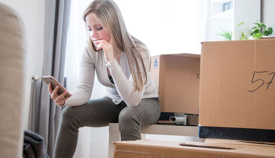 Eine Frau sieht zwischen Umzugskartons auf ein Handy