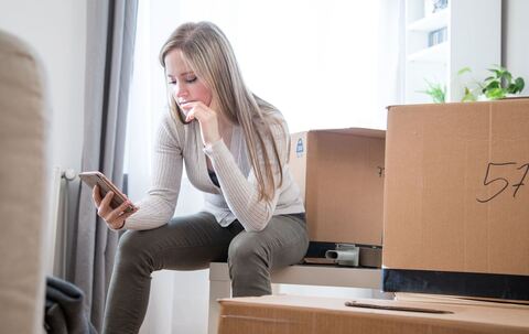 Eine Frau sieht zwischen Umzugskartons auf ein Handy