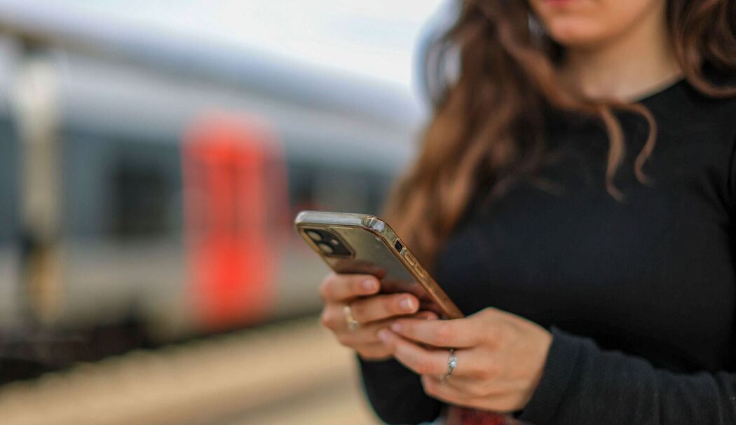 Eine junge Frau steht mit ihrem Mobiltelefon auf einem Bahnsteig Eine junge Frau steht mit ihrem Mobiltelefon auf einem Bahnsteig