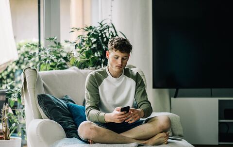Ein junger Mann sitzt mit Smartphone auf einem Sessel