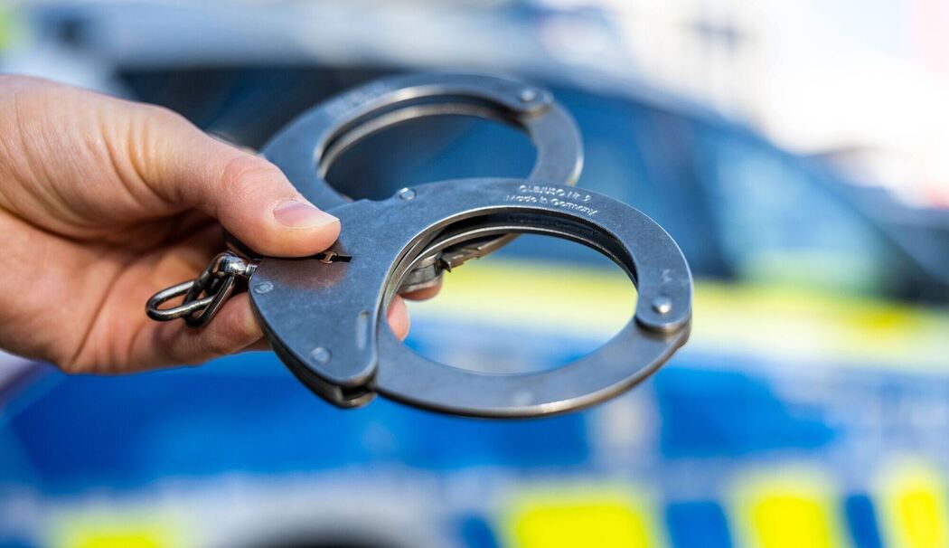 Handschellen vor Polizeiwagen - Symbolbild
