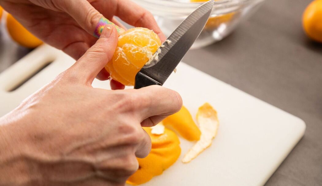 Clementinen werden mit einem Messer von den weißen Fäden befreit Clementinen werden mit einem Messer von den weißen Fäden befreit