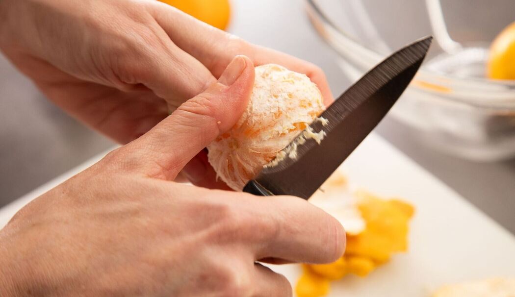 Eine Clementine wird mit einem Messer geschält Eine Clementine wird mit einem Messer geschält