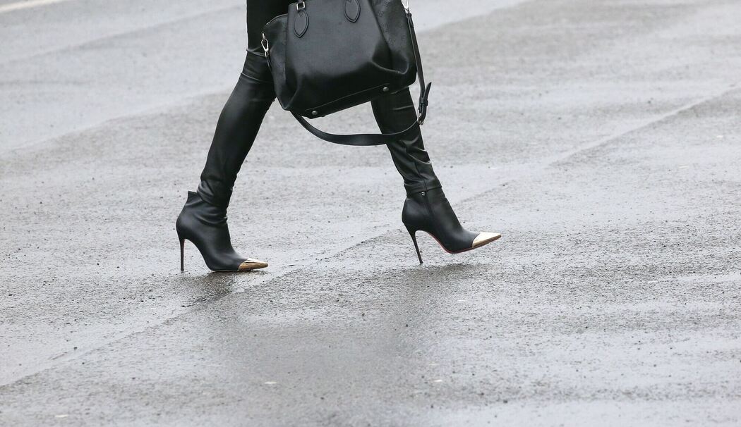 Frau mit High Heels geht über eine regennasse Straße