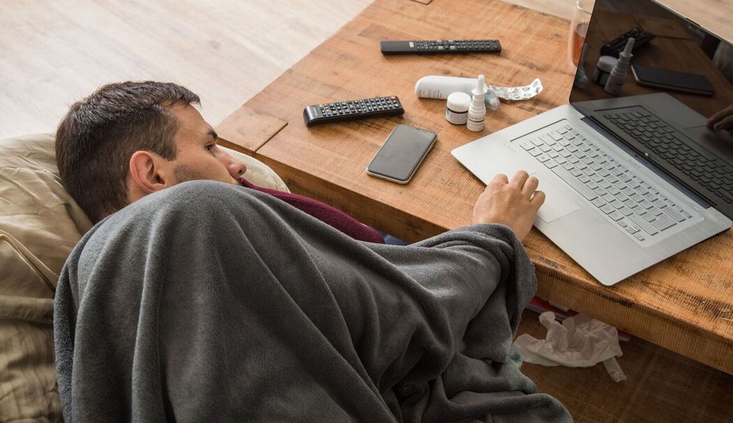 Ein Mann mit Erkltung bedient ein Laptop