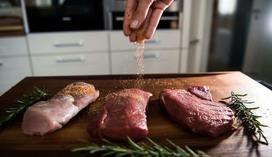 Eine Perosn würzt Fleisch