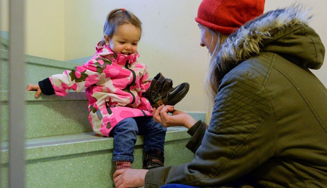 Eine Mutter hilft einem Kleinkind die Schuhe anzuziehen Eine Mutter hilft einem Kleinkind die Schuhe anzuziehen