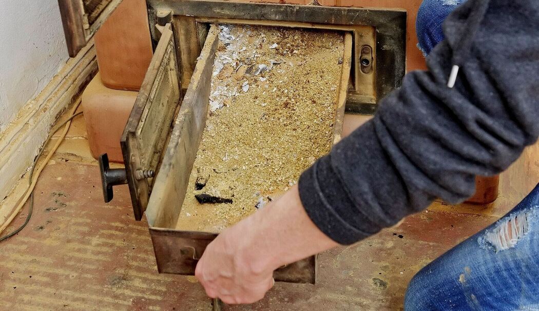 Eine Frau entnimmt die Ascheschublade aus einem Kachelofen