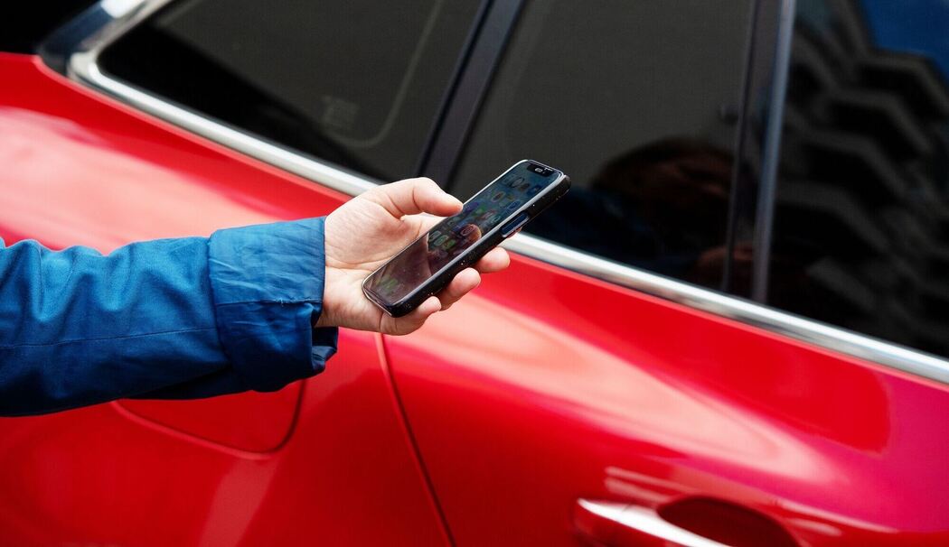 Eine Person steht mit einem Smartphone neben einem Auto