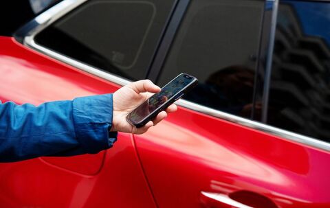 Eine Person steht mit einem Smartphone neben einem Auto