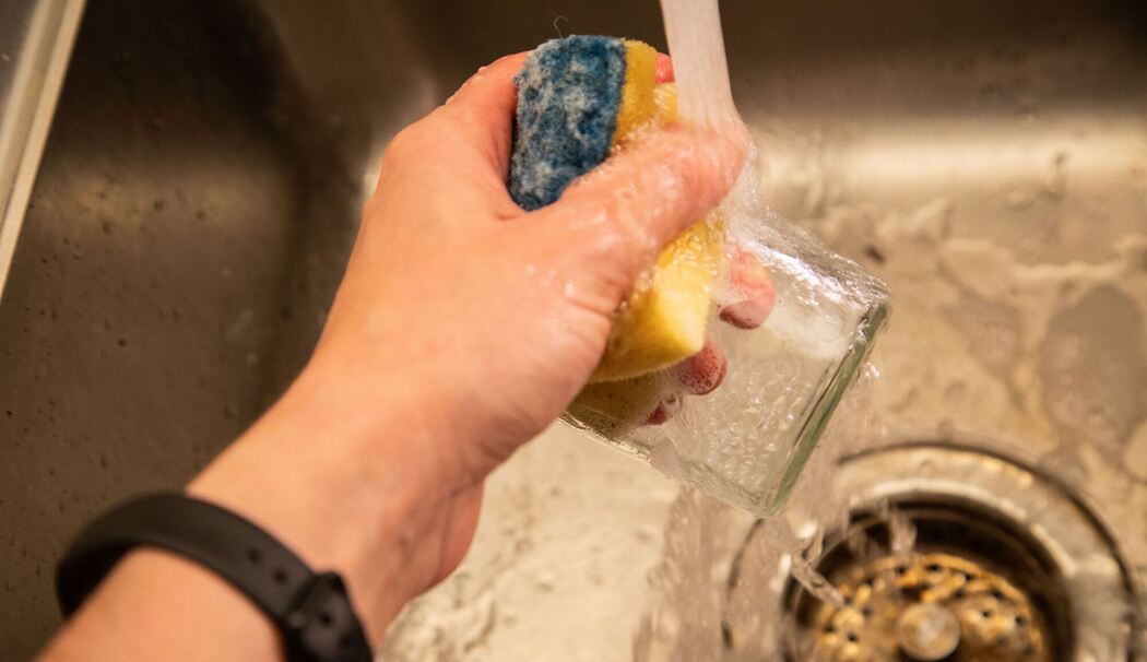 Glas wird mit Spülmittel unter fließendem Wasser gereinigt Glas wird mit Spülmittel unter fließendem Wasser gereinigt