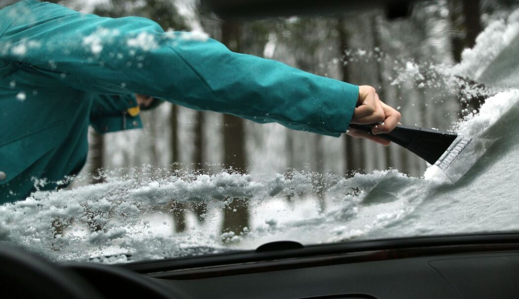 Ein Mann kratzt die verschneiten Scheiben eines Autos frei