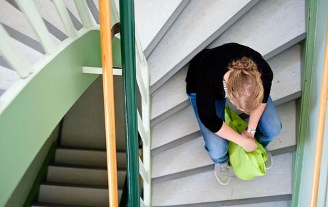 Eine Frau sitzt in einem Treppenhaus auf einer Treppenstufe